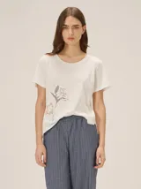 Remera de manga corta color blanco off-white, con cuello redondo y diseño bordado de flores en el lateral inferior.
