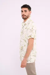 Camisa blanca con estampado de hojas verdes y marrones, de manga corta y cuello clásico.