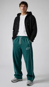 Pantalón jogger verde oscuro de corte holgado, con cordón de ajuste blanco en la cintura, bolsillos laterales con ribete blanco y un pequeño logo bordado en la pierna izquierda.
