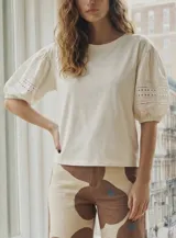 Remera de algodón color blanco, con cuello redondo y mangas abullonadas de largo tres cuartos que presentan detalles de bordado inglés y calados.