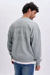 Buzo deportivo oversize verde pastel con cuello redondo, mangas largas y estampa tipográfica en la espalda.