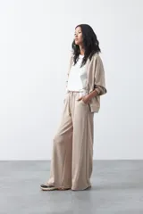 Pantalón de corte holgado y pierna ancha, con cintura elástica ajustable mediante cordón. Presenta bolsillos laterales y costuras verticales decorativas que recorren el frente de las piernas.