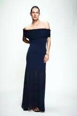 Vestido largo de punto color azul marino, con escote recto tipo off-shoulder con detalle de frunces en la parte superior. Presenta un diseño entallado en el torso y una falda con caída fluida y bajo combinado en tejido semitransparente.