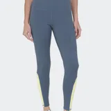 Calza deportiva de tiro alto, color gris azulado, con recortes laterales en amarillo claro. Presenta paneles con microperforaciones en la zona de la cadera y una franja vertical amarilla en la parte inferior de las piernas.