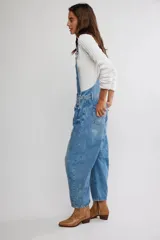 Jardinero enterito de denim en color azul claro, con diseño de peto, tiras regulables y botones laterales. Presenta corte amplio estilo barrel con piernas abuchonadas y bolsillos frontales.