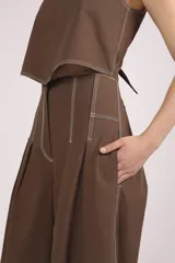 Pantalón marrón de corte palazzo, tiro alto, con pliegues frontales y pespuntes blancos decorativos.