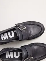 Mocasines de cuero color gris oscuro con diseño de costura en el empeine, ajuste mediante tira con hebilla metálica y suela track con taco de 4 cm.