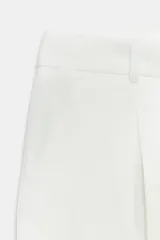 Shorts color beige confeccionados en hilatura con lino, de tiro alto. Presentan bolsillos delanteros, falsos bolsillos traseros con solapa y pinzas delanteras. Cierre frontal con cremallera y gancho metálico.