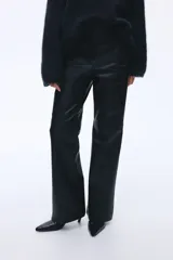 Pantalón de cuero sintético negro con corte bootcut, cierre frontal con botón oculto y costuras decorativas sobre las rodillas.