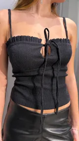 Top negro de tirantes finos con diseño fruncido en nido de abeja en todo el cuerpo, escote recto con volado sutil y cordones ajustables en el centro del busto con detalle de abertura en gota.