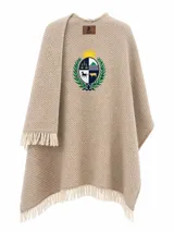 Ruana de hilo de algodón color beige con textura acanalada diagonal, terminaciones con flecos en el ruedo y bordado central del escudo nacional.