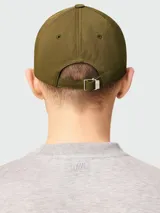 Gorra de béisbol color verde oliva, confeccionada en nylon, con visera curva y un pequeño pin metálico con el logo de corazón de Ami Paris en el frente.