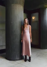 Vestido largo de estilo lencero en tejido satinado color rosado. Presenta escote en pico con detalle de encaje en el pecho y en el bajo, tirantes anchos ajustables y cierre de cremallera lateral.