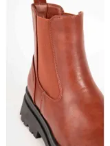 Bota de caña baja tipo Chelsea color marrón, con paneles elásticos laterales y suela track negra con plataforma dentada. Presenta textura en relieve en la parte trasera del talón.