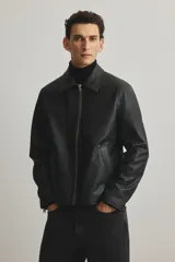 Campera negra de efecto cuero con cuello camisero, cierre frontal y bolsillos laterales con cierre. Presenta un corte estándar y forro interior.