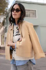 Chaqueta corta tipo blazer color marrón, confeccionada en tela de lana afieltrada. Tiene cuello camisero, silueta cuadrada, cierre frontal con botones y bolsillos delanteros.