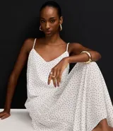 Vestido largo de corte evasé confeccionado en crepé, con escote en V, breteles finos ajustables y detalle de ruedo fruncido. Presenta una estampa clásica de lunares.