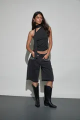 Bermuda de denim negro con diseño holgado, tiro medio y detalles de tachas y strass aplicados en los bolsillos delanteros. Presenta terminaciones deshilachadas en las piernas.
