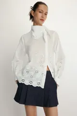Camisa de manga larga en color blanco, confeccionada con detalles de bordados perforados a tono. Presenta un cuello tipo pañuelo y cierre frontal con botones.