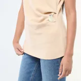 Sweater sin mangas color beige de tejido de punto, con cuello alto y detalle de hebilla metálica en forma de corazón en el lateral de la cintura.