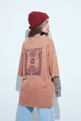 Remera de corte oversize color marrón con efecto gastado, manga corta y estampa gráfica retro en el frente.