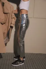 Pantalón de ecocuero metalizado color plateado, de corte capri semi oxford y tiro medio-alto. Presenta cierre frontal con botón metálico y costura horizontal a la altura de la rodilla.