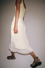 Falda midi de tiro medio, color beige, con detalle de combinación de tejidos a contraste y volante plisado semitransparente en el bajo. Cuenta con cierre lateral de cremallera oculta.