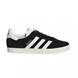 Championes urbanos Adidas modelo Gazelle, color negro con las icónicas tres tiras laterales y refuerzo en el talón en color blanco. Presenta el nombre del modelo en letras doradas en el lateral y suela de goma texturizada en color crema.