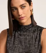 Blusa sin mangas de poliéster satinado color negro con estampado geométrico de líneas blancas y cuello alto drapeado.