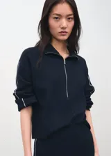 Jersey de punto color negro, con cuello polo y cierre frontal de cremallera, mangas largas y detalles de ribetes claros en las costuras.