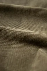 Camisa de manga larga confeccionada en pana de algodón, color verde oliva. Presenta cuello con botones, cierre frontal abotonado y un bolsillo en el pecho con etiqueta pequeña.