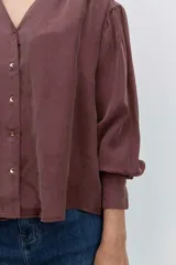 Camisa de satén color azul grisáceo, con cuello mao con detalle de volados, cierre frontal con botones y mangas largas con puños abotonados.