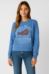 Buzo de cuello redondo y manga larga en color azul, con estampado frontal que incluye texto y un diseño de langosta.