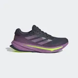 Championes de running Adidas Supernova Rise para mujer, con capellada de malla en tonos gris oscuro y morado, tres franjas moradas y detalles en amarillo neón. La mediasuela es gruesa, predominantemente morada con una capa de amortiguación en amarillo neón que lleva la inscripción "DREAMSTRIKE+".