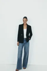 Blazer cruzado color beige, de manga larga, con cuello solapa y forro interior negro. Presenta cierre frontal con botones dorados y bolsillos de vivo en el pecho y bolsillos con solapa en el delantero.