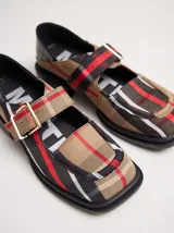 Zapatos tipo guillermina con punta cuadrada, confeccionados en lona resistente con estampado de cuadros escoceses en tonos beige, rojo y negro. Presentan una correa ajustable con hebilla metálica color bronce y una suela con taco de 4 cm.