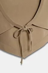 Top sin mangas de algodón color tostado, con cuello redondo y detalle de tachas metálicas en la parte frontal. Presenta un diseño con bajo asimétrico en punta.