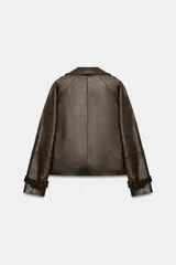 Cazadora de Zara Woman Collection confeccionada en material efecto piel color marrón oscuro. Presenta cuello con solapas, cierre frontal cruzado con botones, bolsillos delanteros y mangas largas con trabillas y hebillas ajustables en los puños.