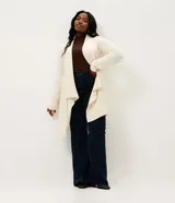 Cardigan de punto color marrón, con diseño alargado y puntas asimétricas. Presenta mangas largas, cuello tipo chal y detalles de textura canelada en los laterales.