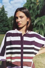 Camisa blanca de corte oversize y largo midi, confeccionada en algodón. Presenta cuello mao, cierre frontal oculto por tapeta y mangas cortas con dobladillo. Incluye un pequeño bordado de una flor en el pecho.