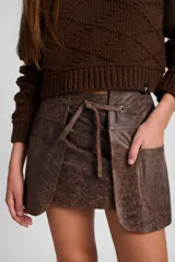 Minifalda de cuero con efecto desgastado, de silueta recta y diseño de capas frontales superpuestas. Incluye un lazo ajustable en la cintura que pasa por ojalillos metálicos y bolsillos laterales integrados.