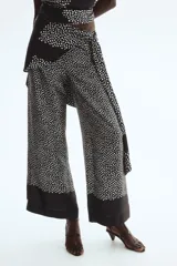 Pantalón negro con estampado de lunares blancos, corte recto y falda cruzada superpuesta con lazada en el lateral.