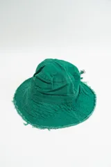 Gorro tipo bucket color verde, con ala ancha y bordes deshilachados. Incluye una pequeña hebilla metálica decorativa en el lateral.