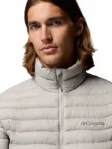 Campera puffer híbrida Columbia modelo Powder Pass Hybrid, de color gris claro con paneles laterales en tono marrón oscuro. Cuenta con cuello alto, cierre frontal completo y bolsillos laterales con cierre. Logo de la marca bordado en el pecho.