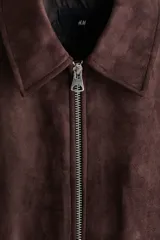 Campera marrón de tejido suave con acabado cepillado, cuello camisero, cierre frontal y bolsillos laterales.