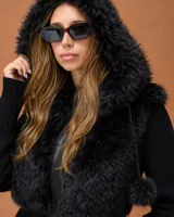 Campera de diseño combinado con cuerpo en textura de piel sintética y mangas tejidas. Presenta una capucha amplia con borde de pelo sintético y cierre frontal.