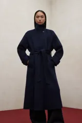 Abrigo largo de lana reciclada en color azul marino, con diseño de cuello alto, mangas raglán y cinturón ajustable a la cintura. Presenta un corte elegante y minimalista con cierre frontal oculto.