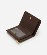 Billetera mediana color marrón, confeccionada en poliuretano con textura lisa y detalle de gamuza en la parte superior. Presenta cierre superior con cremallera dorada y aplicación de tachas metálicas decorativas en el frente.
