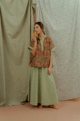 Blusa de algodón con estampado floral multicolor, con detalles en tela a cuadros verde y blanca en el cuello en V, la pechera y los bordes de las mangas cortas.