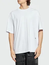Remera blanca de algodón con cuello redondo y corte oversize. Presenta un pequeño detalle rectangular negro en la parte inferior delantera.